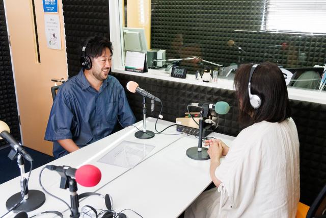 写真：ラジオ局のブースでマイクを前にトークする男女のパーソナリティ
