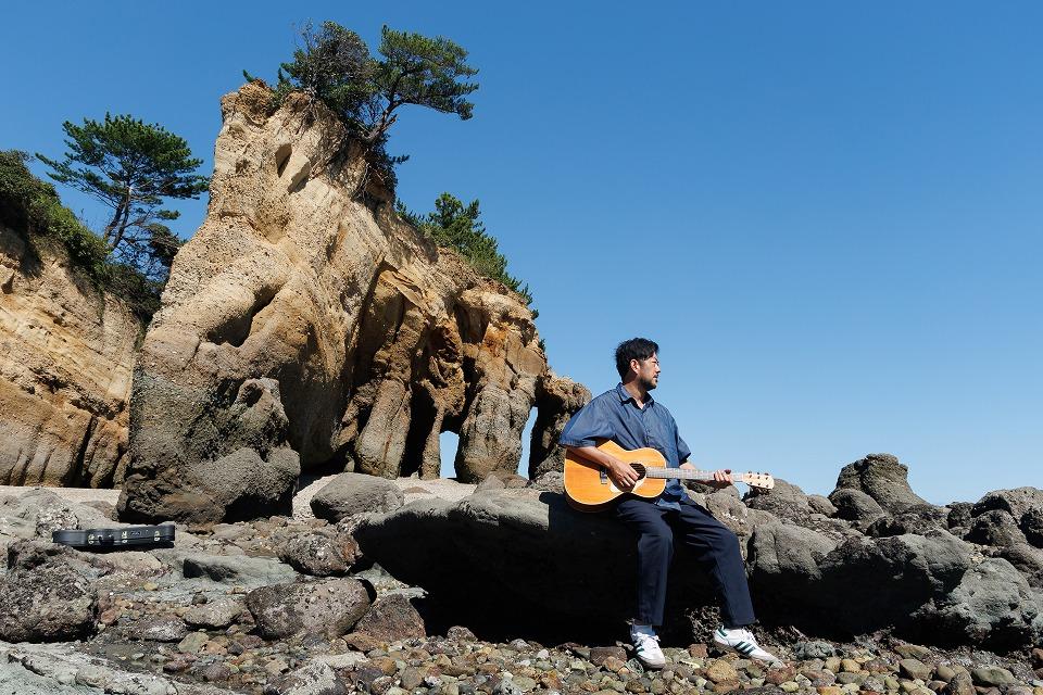写真：岩場でギターを弾く男性。